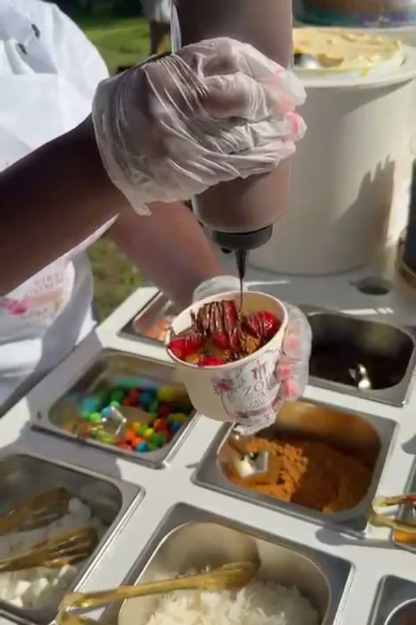 Hand finishing a dessert cup with chocolate sauce and toppings