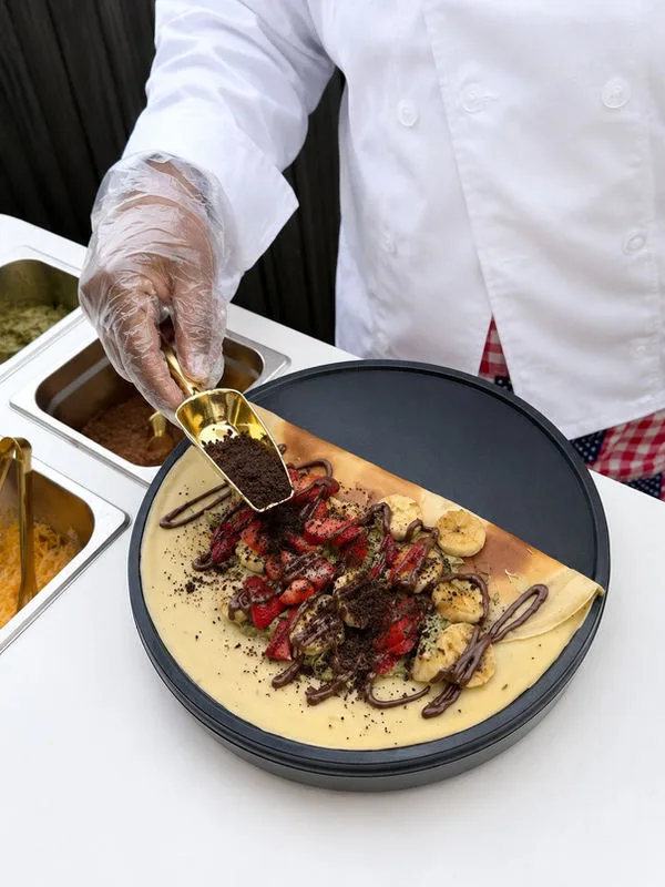 Caterer adding fruit and chocolate to a crepe on the griddle